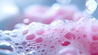 Pink and white soap bubbles in macro photography with soft bokeh effect and delicate foam texture creating abstract background for cosmetic and hygiene products.