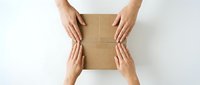 Overhead view of multiple hands holding and opening a kraft cardboard box on white surface, representing delivery, unboxing, and package handling.