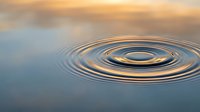 Concentric water ripples spreading across calm surface with golden sunset reflection creating peaceful zen meditation atmosphere for wellness concepts.