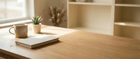 Minimalist wooden desk workspace with coffee mug, notebook and small potted plant in bright natural sunlight for home office productivity and organization.