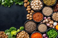 Variety of legumes, nuts, vegetables and healthy plant protein sources in bowls on dark background with copy space for menu or recipe design.