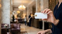 Concierge in formal attire holding blank key card in luxury hotel lobby with elegant interior and warm lighting.