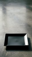 Empty black and white rectangular tray on concrete surface with dramatic shadow, suitable for food styling, product photography, and minimalist design projects.