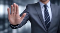 Businessman in gray suit showing stop gesture with palm of hand, representing authority, boundary setting, or rejection in professional environment.