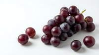 Fresh red grapes cluster with scattered berries on white background, organic fruit for healthy eating and cooking recipes.