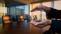 Business professional hands protecting digital house model with network connections in modern office environment for real estate technology concepts.