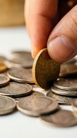 Hand holding vintage gold coin among scattered antique silver coins on white surface, representing numismatic collecting, investment, and financial wealth.