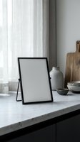 Empty black photo frame on marble kitchen counter with ceramic bowls and cutting board in modern minimalist interior design setting.
