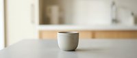 Minimalist ceramic cup with lid on white countertop in modern kitchen setting, suitable for home decor, lifestyle, and product photography projects.