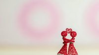 Red decorative couple figurines embracing on soft pink bokeh background for romantic Valentine's Day celebration and love themed designs.