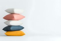 Stack of colorful decorative pillows in white, coral pink, teal blue and yellow against white wall background, minimal interior design composition.
