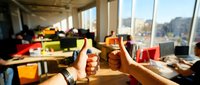Diverse team of professionals collaborating in modern office space with city skyline views, holding coffee cups during work meeting or brainstorming session.