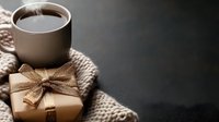 Cozy winter composition with hot coffee cup, knitted scarf and wrapped gift box with golden bow on dark background. Perfect for seasonal greeting cards.