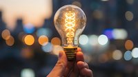 Hand holding glowing vintage Edison bulb against blurred city lights at dusk. Creative innovation and bright ideas concept for business and inspiration.