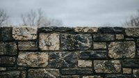 Ancient weathered stone wall with mixed gray and beige blocks showing natural texture and aging patterns against overcast sky for rustic architectural backgrounds.