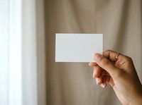 Hand holding blank white business card against neutral beige background, suitable for branding, corporate identity, and marketing mockup presentations.