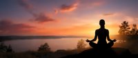 Silhouette of person meditating in lotus pose during golden sunset over calm lake with colorful sky and peaceful natural landscape for wellness content.
