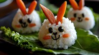 Playful bunny-shaped rice balls decorated with carrots, olives, and nori on lettuce leaves create fun Easter or children's party food presentation.