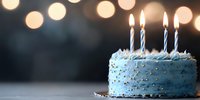 Blue birthday cake with lit candles against dark background with soft bokeh lights creating festive atmosphere. Celebration moment captured in minimal style.