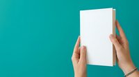 Female hands with manicured nails holding blank white book or magazine against turquoise background, suitable for publishing, marketing, and product mockup designs.