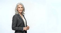 Mature woman with silver-gray hair, Caucasian ethnicity, wearing professional black blazer over white shirt. Corporate executive portrait for business, leadership, and professional services marketing.