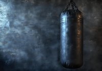 Black boxing bag hanging against dark textured background, dramatic lighting creates moody atmosphere for sports and fitness concepts.