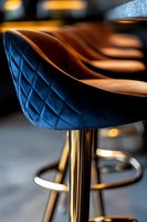 Luxurious quilted blue velvet bar stool with brown leather seat and gold metal base, modern restaurant furniture detail with soft bokeh background.