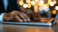 Professional businessman typing on laptop computer with warm bokeh lights in background creating cozy evening work atmosphere for business presentations.