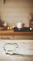 Sheep-shaped cookie cutter on flour-dusted wooden surface with warm kitchen background and bokeh lights, suitable for baking and cooking content.