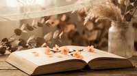 Open book with autumn leaves on wooden table surrounded by dried pampas grass and eucalyptus branches creating cozy seasonal reading atmosphere for fall decor.