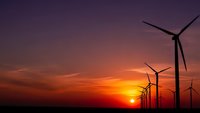 Wind turbines silhouetted against dramatic sunset sky with orange and purple hues creating renewable energy landscape for sustainable power generation.