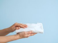 Person holding folded white towel or cloth against light blue background for hygiene, cleaning, laundry, and household product advertising.