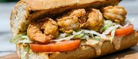 Crispy fried shrimp po boy sandwich with fresh lettuce and tomato on crusty French bread roll, perfect for restaurant menus and food delivery apps.