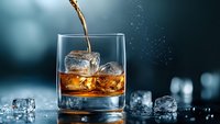 Whiskey pouring into glass with ice cubes on dark background with water drops and bokeh lights, dramatic beverage photography for bar and restaurant menu.