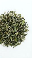 Dried green tea leaves and buds scattered on white background, suitable for beverage, wellness, and culinary product packaging.
