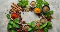 Aromatic spices and fresh herbs arranged in circular pattern on rustic stone surface. Cinnamon sticks, star anise, turmeric, cumin seeds and mint leaves for cooking.