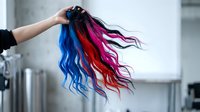 Hand holding colorful hair extensions in blue, red, and magenta shades. Isolated on white background, ready for beauty and fashion design use.