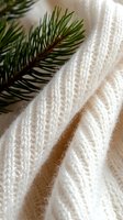 Cozy white knitted wool texture with pine branch, creating winter holiday atmosphere. Soft fabric details showcase delicate stitching pattern and natural fibers.