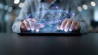 Businessman holding holographic atom model with glowing orbital rings above tablet device. Digital technology concept for science education and innovation.