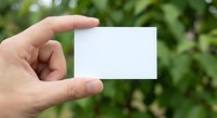Hand holding blank white business card mockup against green blurred nature background for branding and corporate identity design presentations.