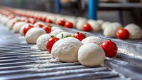 Fresh mozzarella cheese balls and cherry tomatoes on industrial conveyor belt in food processing facility for caprese salad preparation.
