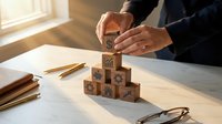 Businessman building wooden block tower on desk representing strategic planning and business growth concepts in modern office environment.