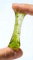Close-up of stretchy green slime being pulled between two fingers, showing texture and translucent quality. Isolated on white background, suitable for educational content, toy product marketing, and children's activity materials.