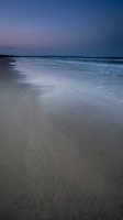 Serene twilight beach scene with gentle waves washing over smooth sand creating peaceful coastal atmosphere for meditation and relaxation concepts.
