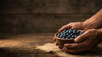 Farmer's hands holding fresh blueberries in wooden bowl on rustic table, harvest and agriculture concept for food production and organic farming.