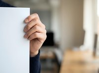 Close-up of hand holding blank white card or paper in office environment for business messaging, advertising, or promotional content display.