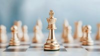 Golden chess king piece standing on chessboard with blurred chess pieces in background, representing leadership, strategy and business success concept.