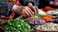 Hands preparing fresh ingredients with colorful bowls of chopped herbs, purple onions, carrots, and legumes for cooking traditional cuisine. Food preparation process.