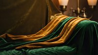 Luxurious emerald green and golden yellow silk fabric draped elegantly with warm candlelight creating rich textures for premium interior design concepts.
