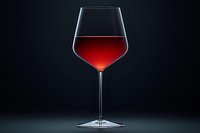 Elegant burgundy wine glass with dramatic backlighting against dark background showcases rich red color and sophisticated stemware design for luxury beverage photography.